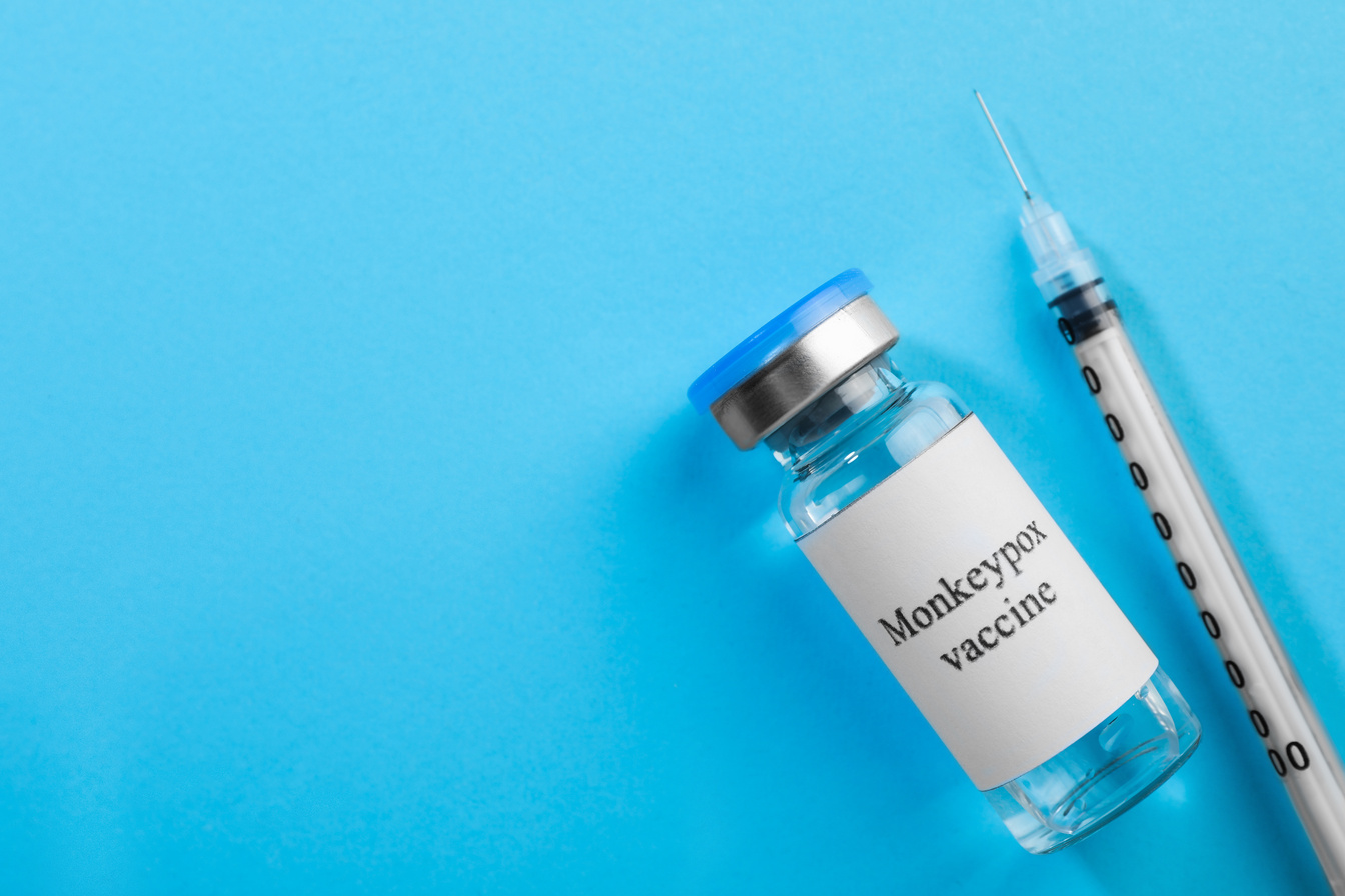 Monkeypox Vaccine in Glass Vial and Syringe on Light Blue Background, Flat Lay. Space for Text